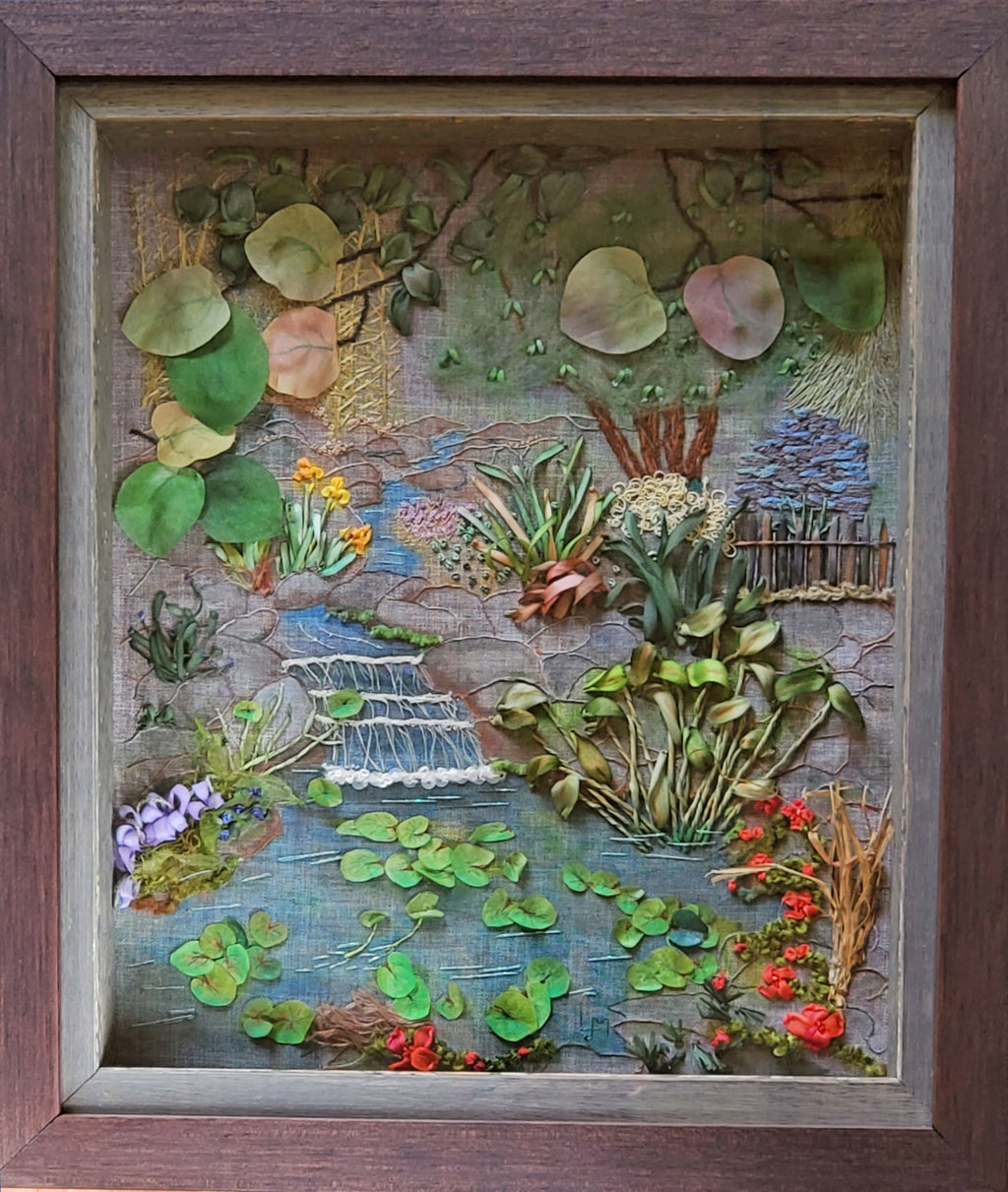 Artistic depiction of a garden scene with plants, flowers, and a stream inside a wooden frame.