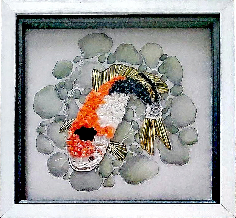Decorative fish art piece on pebbles with a white frame