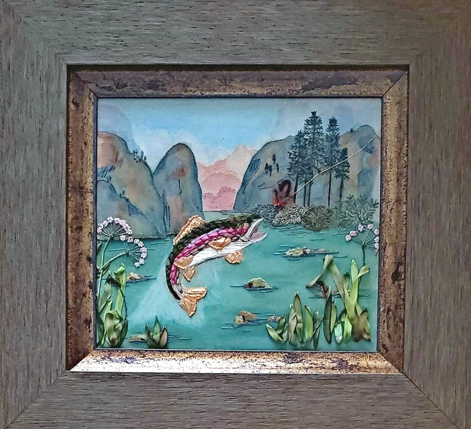 Artistic depiction of a fish in a natural setting with mountains and trees, framed in wood.