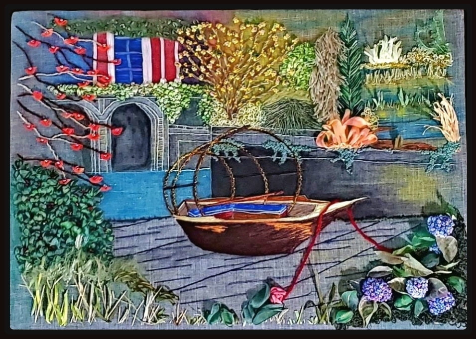Embroidered scene with a boat, flags, and garden elements on a textured fabric background.