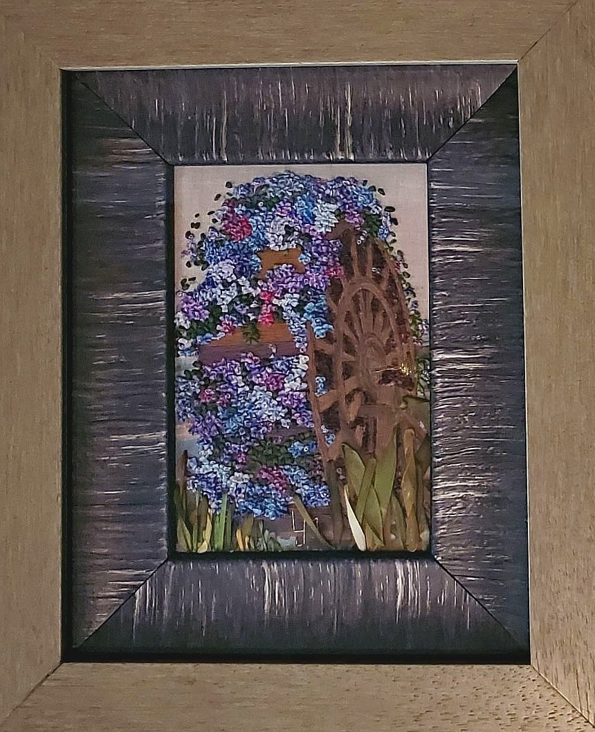 Framed artwork with a colorful floral design and wooden wheel.