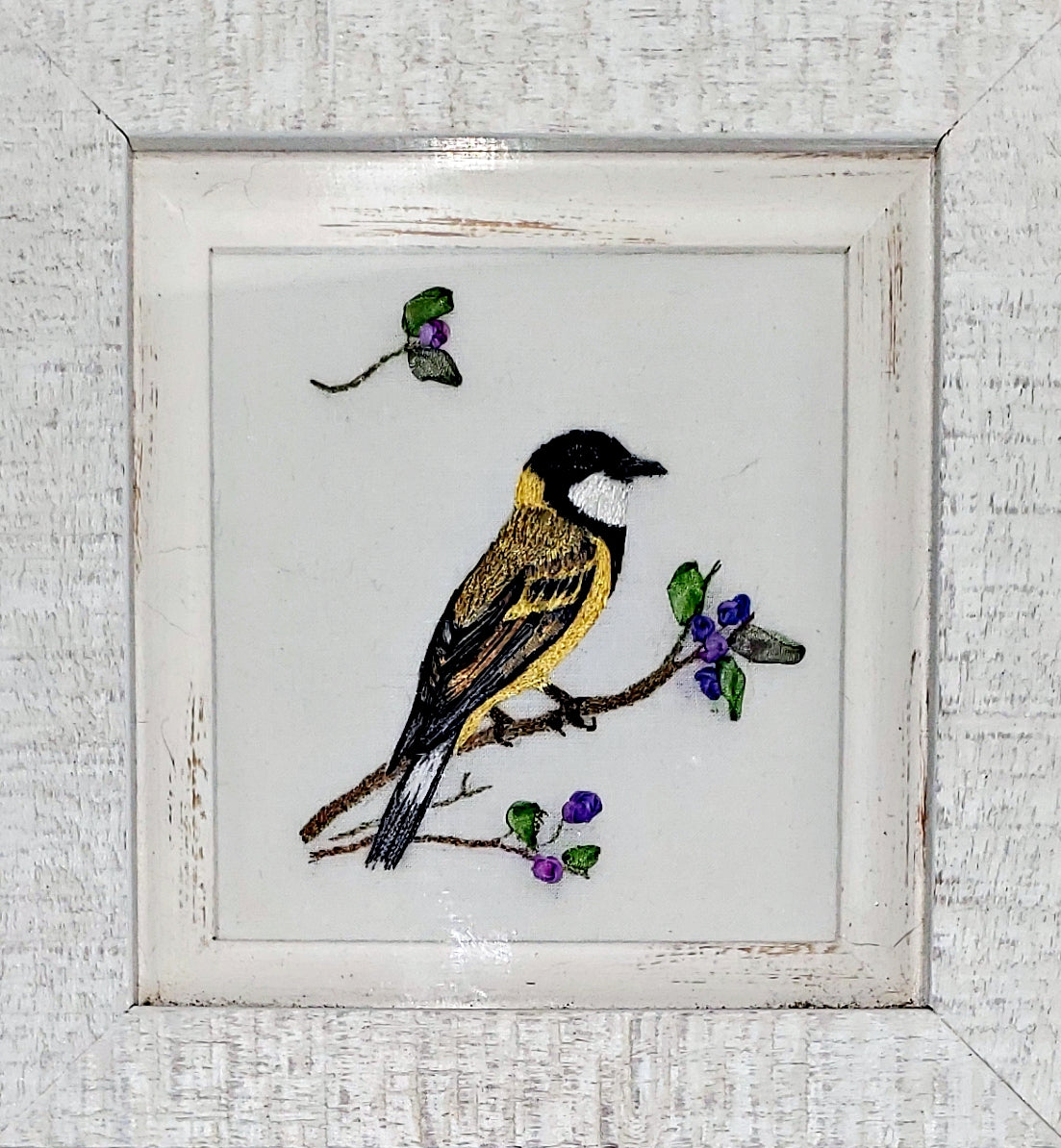 Embroidered picture of a bird on a branch with berries in a white frame.